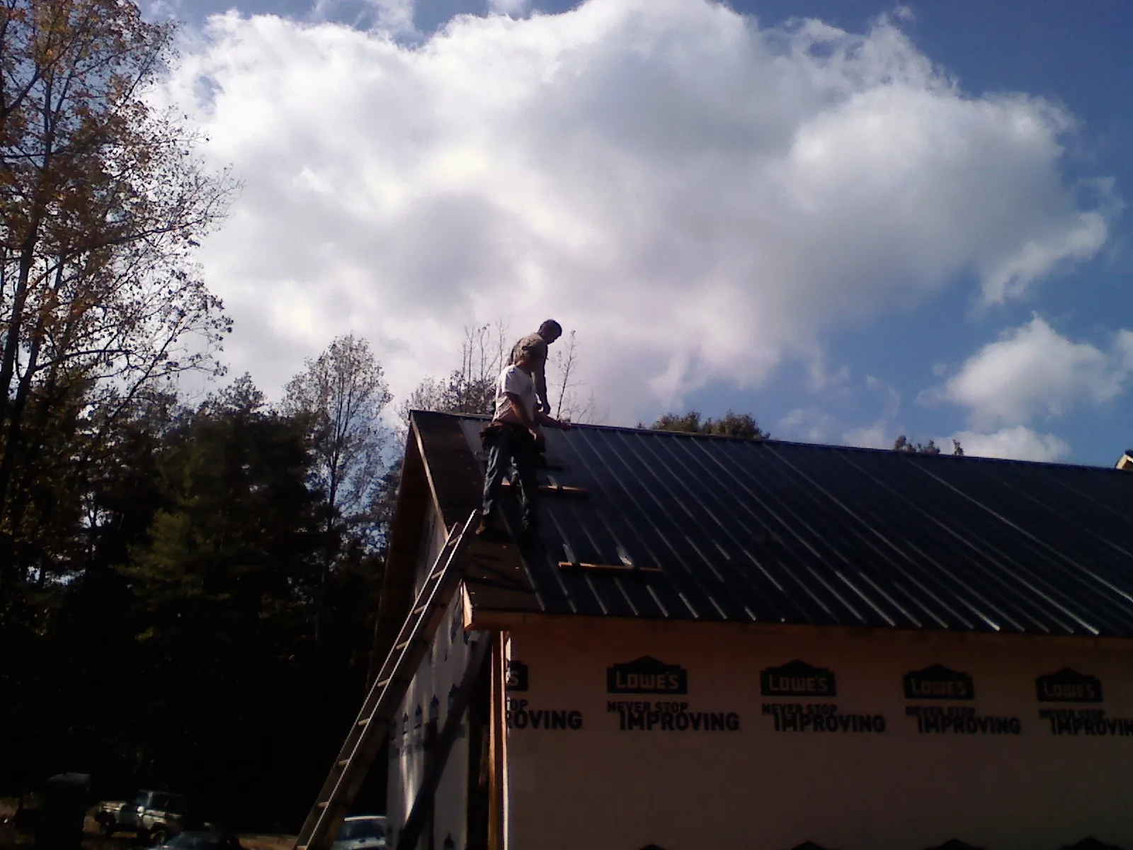 Roofer fastening dark metal panels high against a cloudy sky, from a Roof Inspection job in Morrison